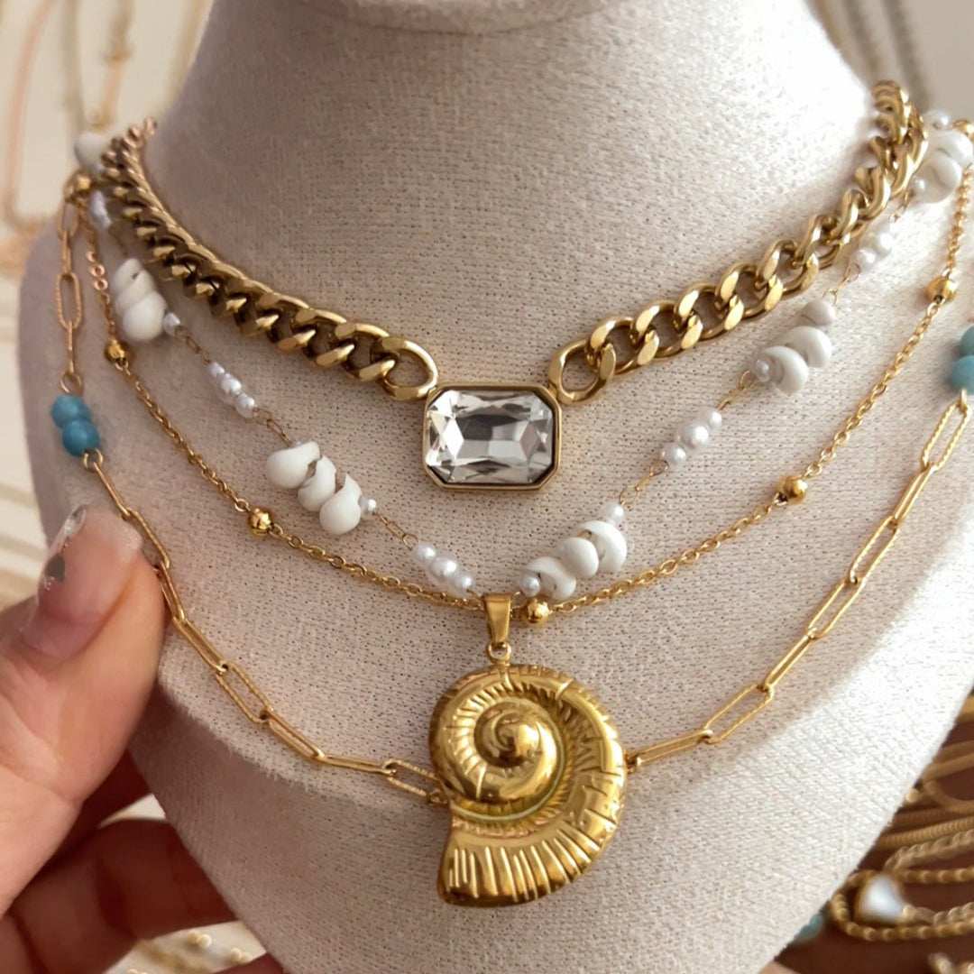 Layered gold-tone necklace set featuring nautilus pendant, crystal charm, and shell beads